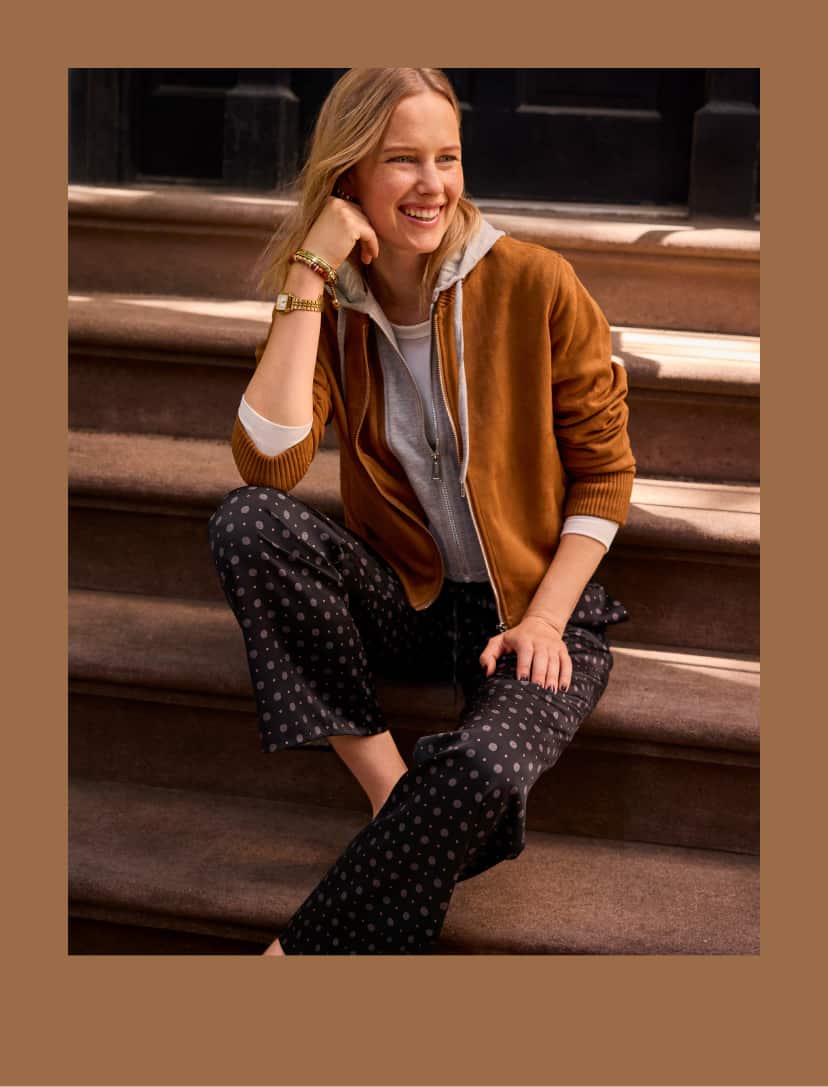 Woman wearing a suede jacket with a grey hoodie and printed satin pants.