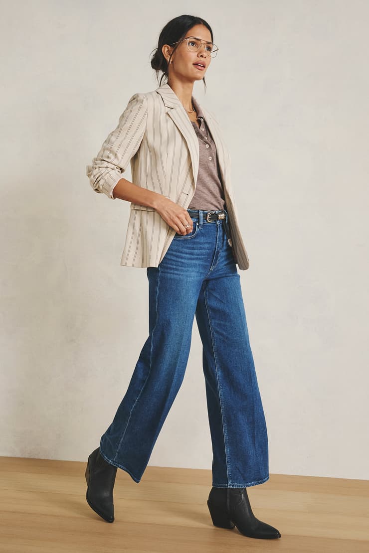 Image of woman wearing stripe blazer over a tan henley, wide leg jeans, and black boots.