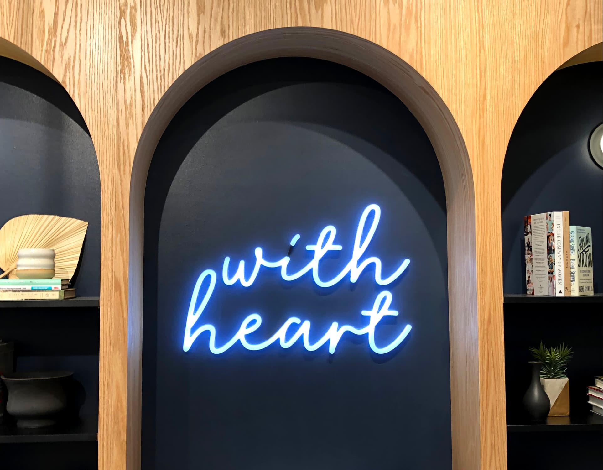 Neon sign with the text 'with heart' in a room with shelves and decor.