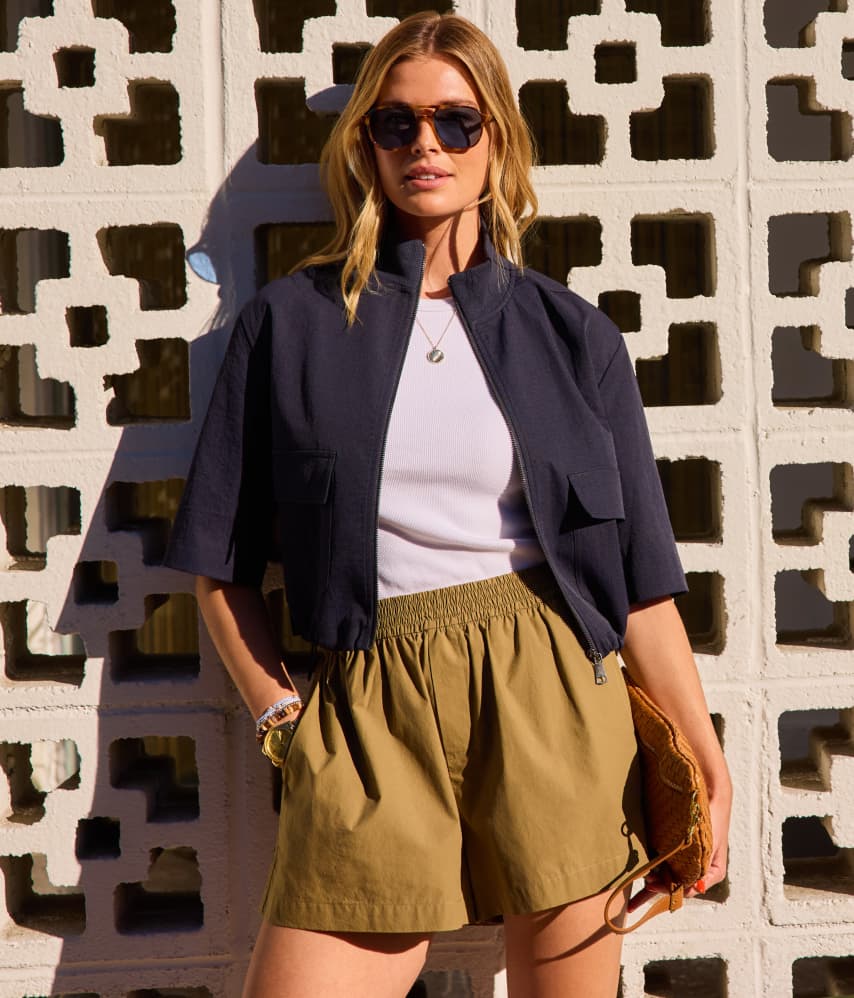 Image of woman in short sleeve navy jacket with white tee and khaki shorts. 