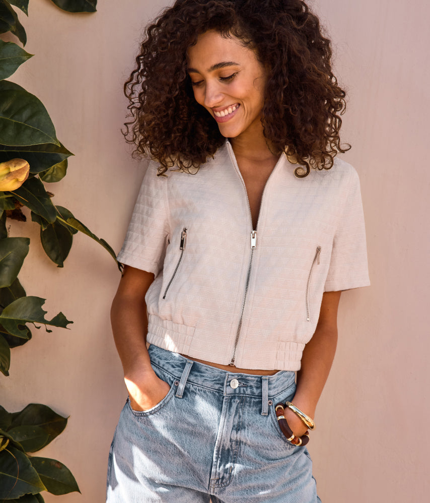 Image of woman wearing an ivory short sleeve zip up jacket with jeans
