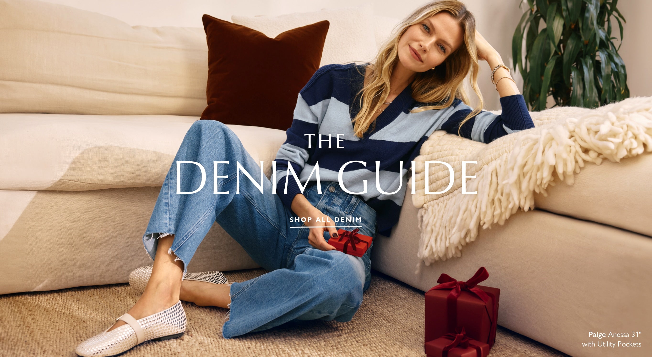 Woman seated on the floor beside a couch wears a navy and blue stripe rugby shirt with wide leg blue jeans and silver studded ballet flats.