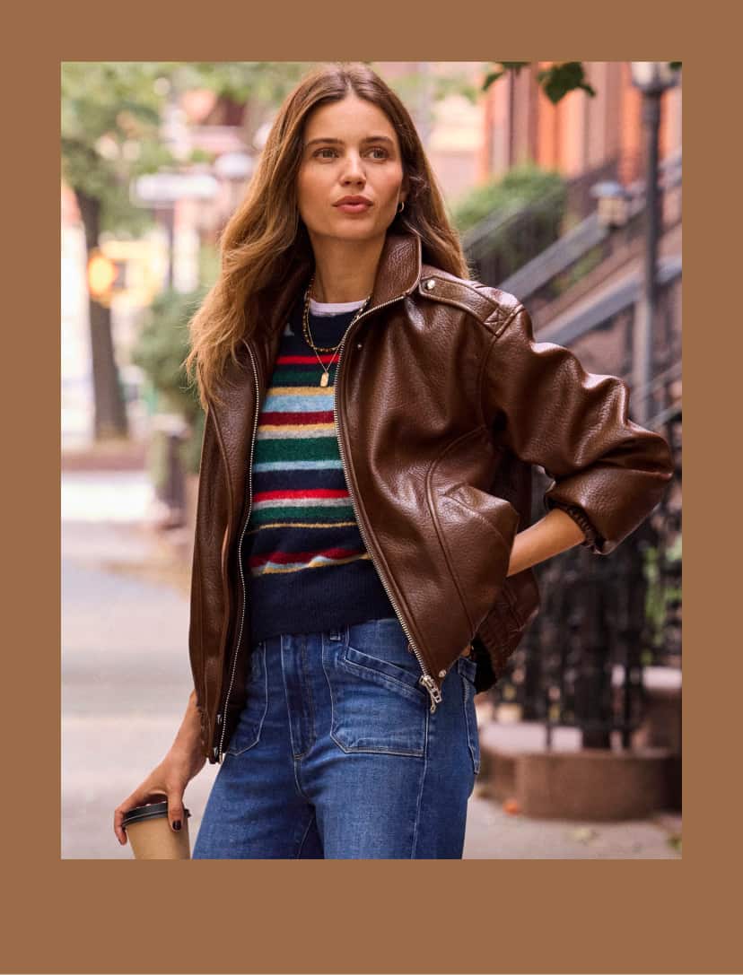 Woman wearing wide leg jeans with a stripe sweater and brown bomber jacket.