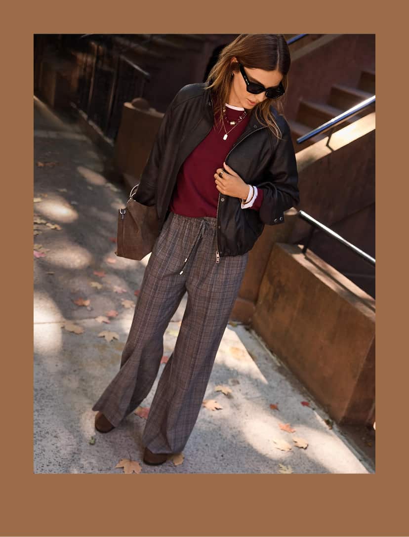 Woman wearing a burgundy sweater with a black bomber jacket and plaid pull-on pants. 