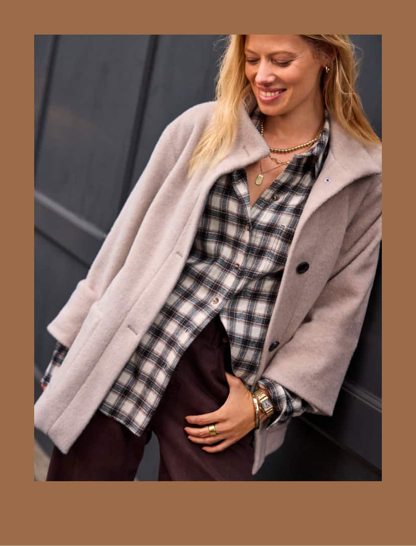 Woman wearing dark brown jeans with a laid shirt and ivory wool overcoat. 