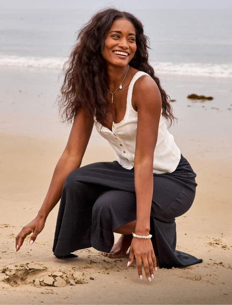 Image of woman on the beach wearing a white tank and black maxi skirt. 