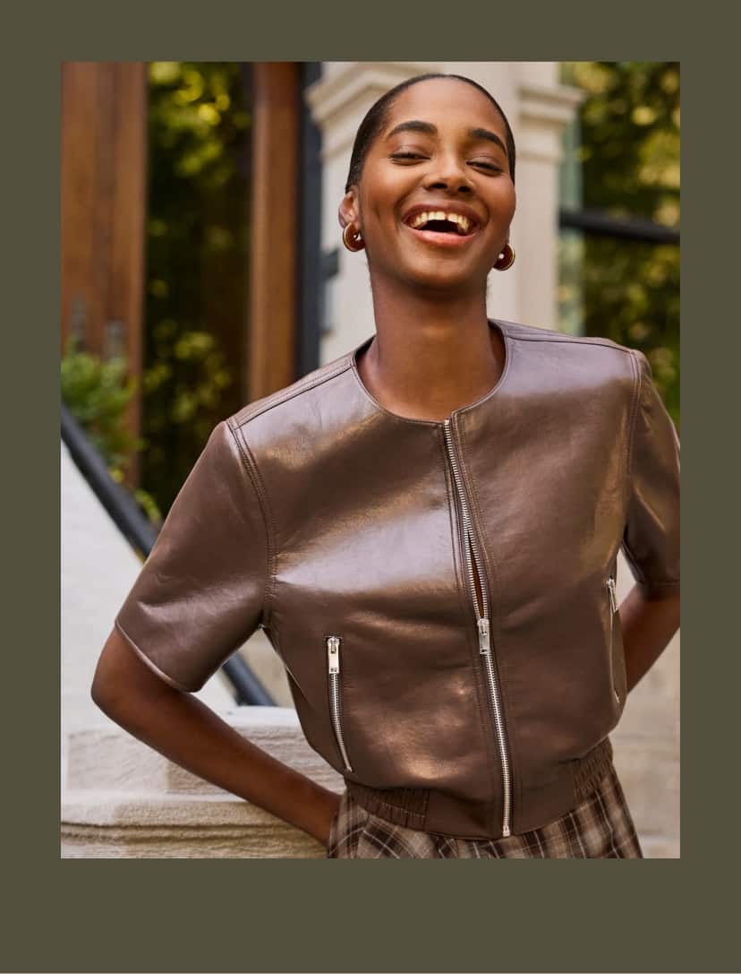 Woman wearing a short sleeve brown leather bomber jacket and plaid skirt. 
