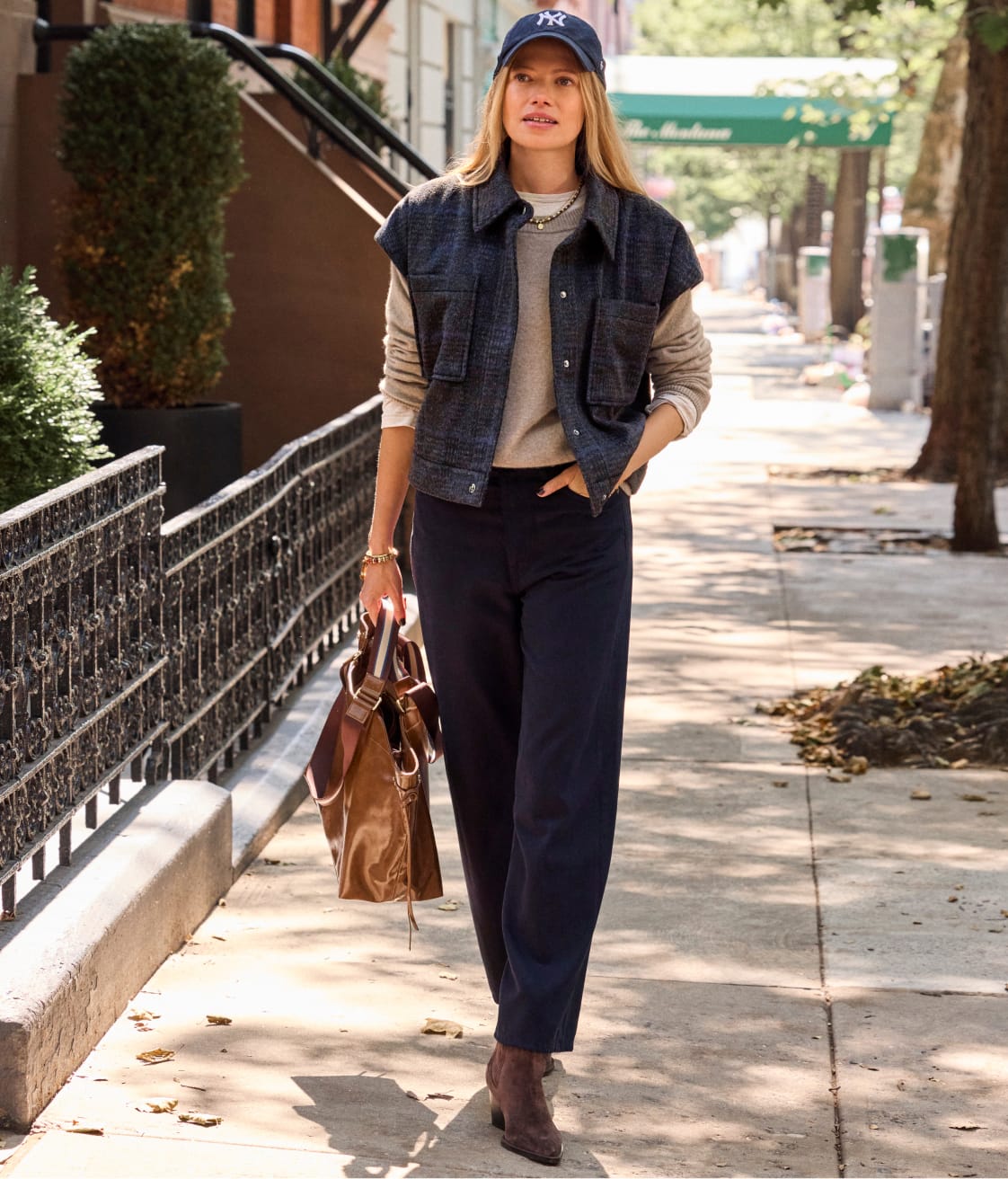 Woman wearing navy pants, tan sweater, and navy sleeveless jacket