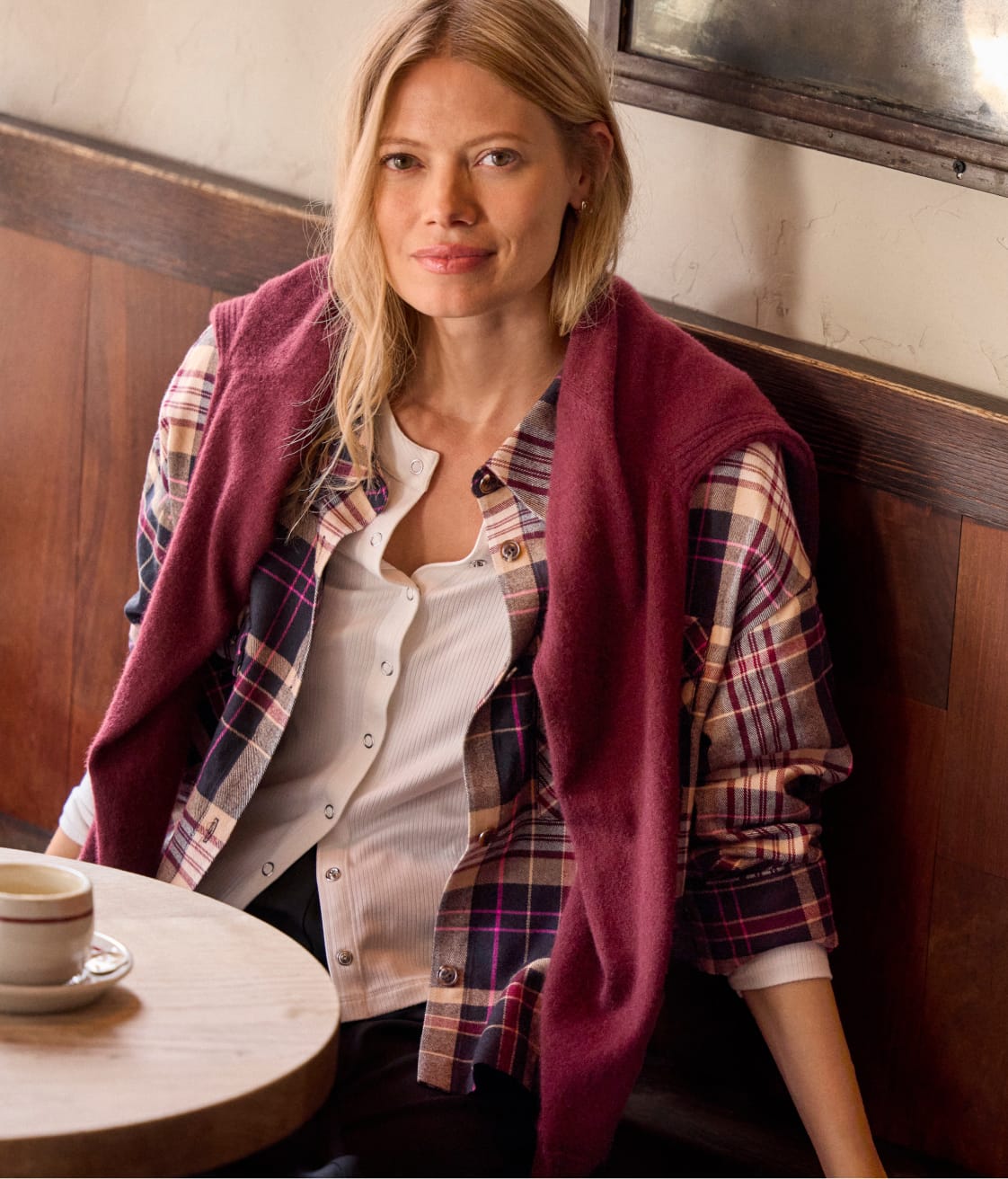 Woman wearing a plaid button down shirt with a maroon sweater over her shoulders