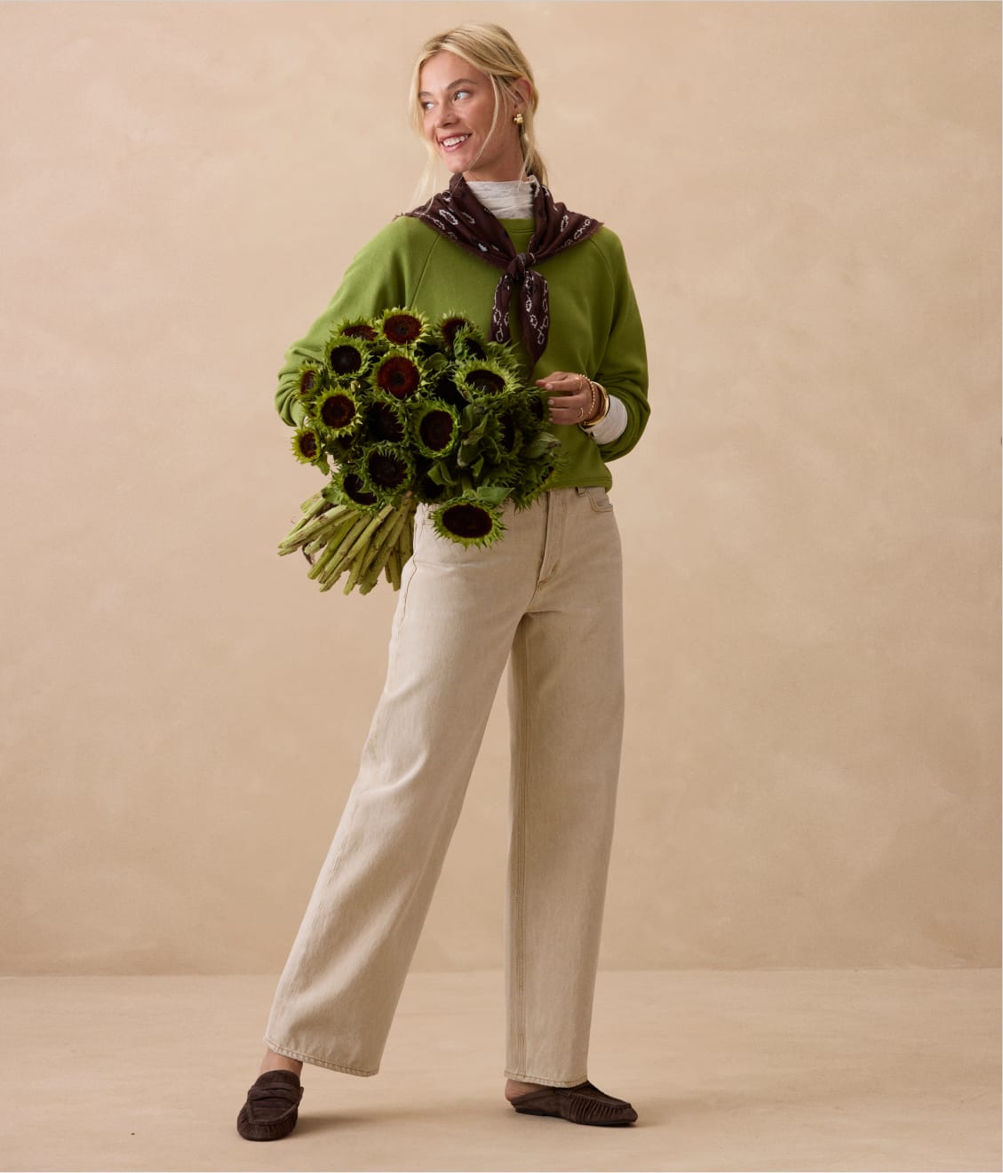 Woman wearing chartreuse pullover sweatshirt with a scarf around her neck and taupe jeans