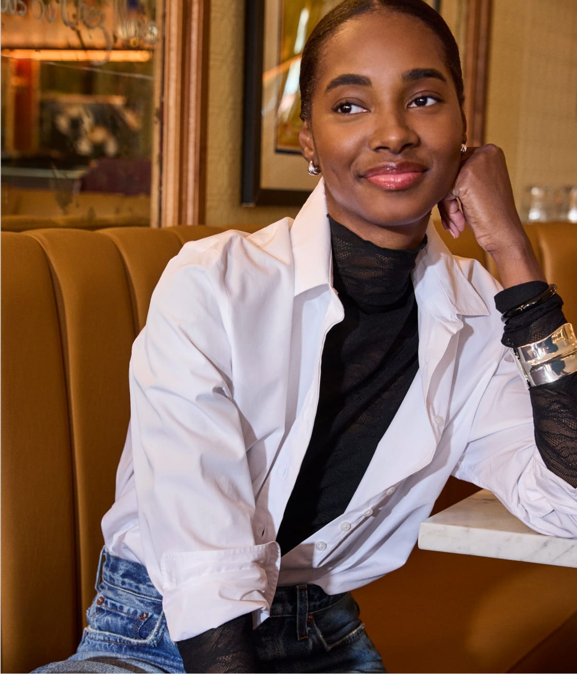 Woman wearing a black lace long sleeve top under a white button down shirt with jeans.