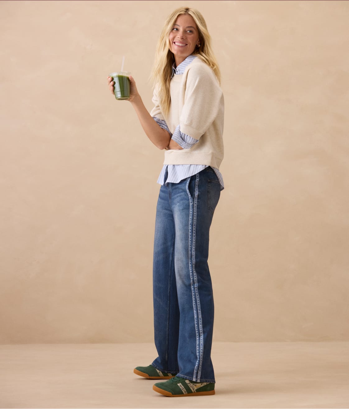 Woman wearing cream crew neck sweatshirt with track stripe blue jeans and sneakers