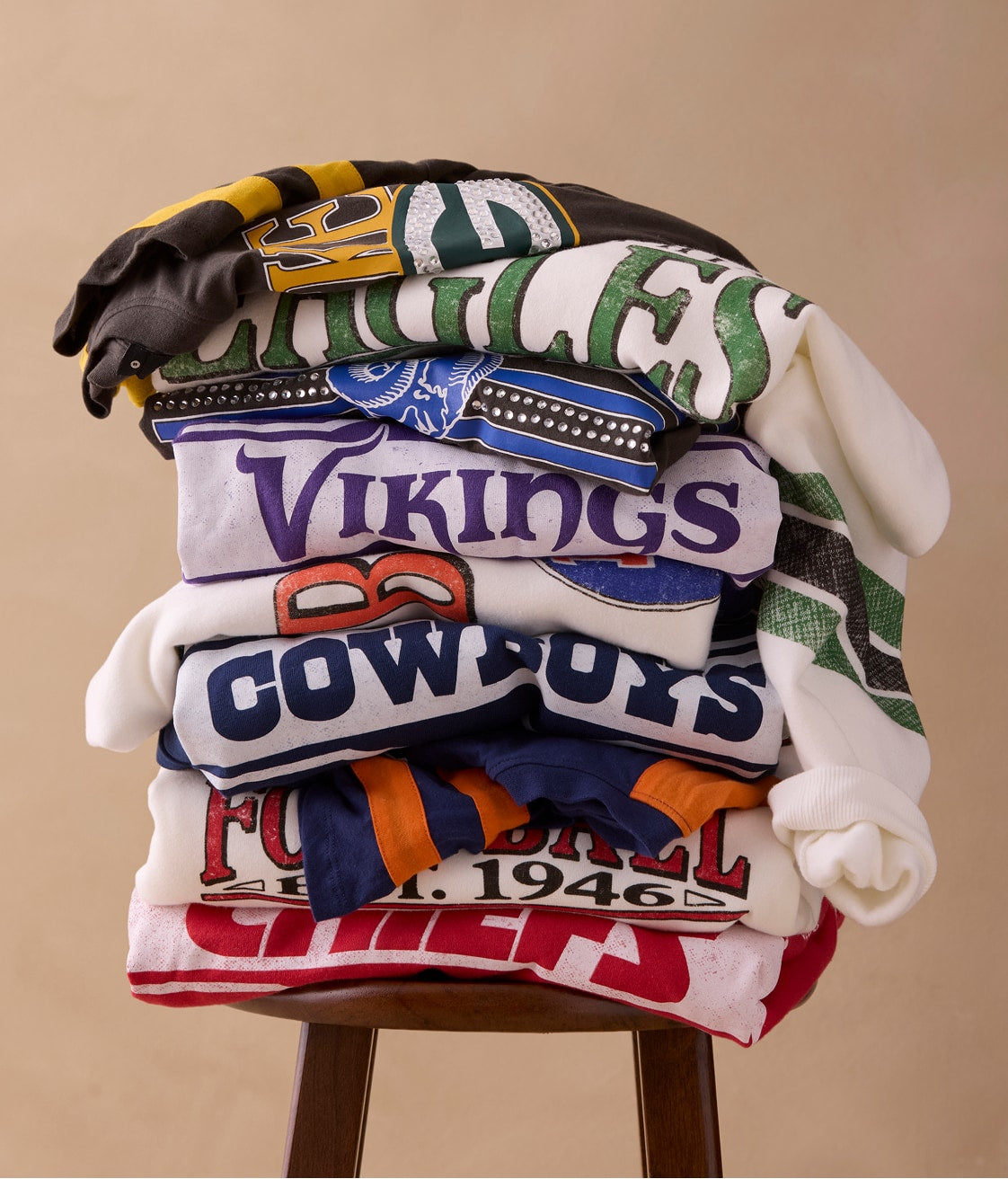 Stack of t-shirts and sweatshirts with football team logos on them. 
