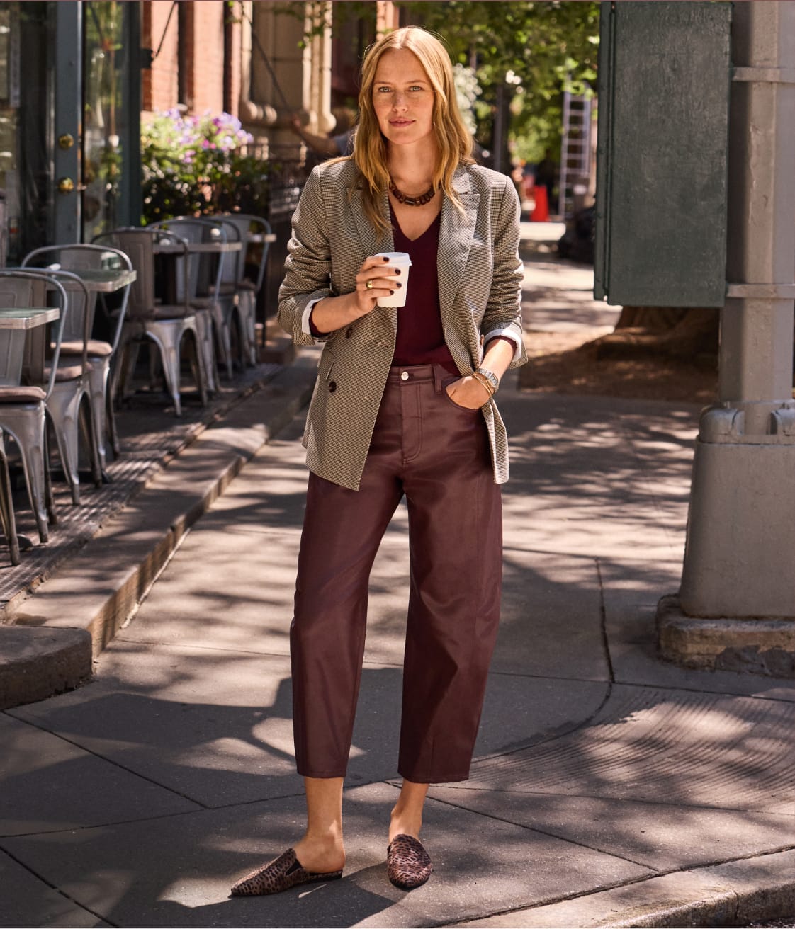 Woman wearing coated barrel leg pants with slides and a brown blazer.