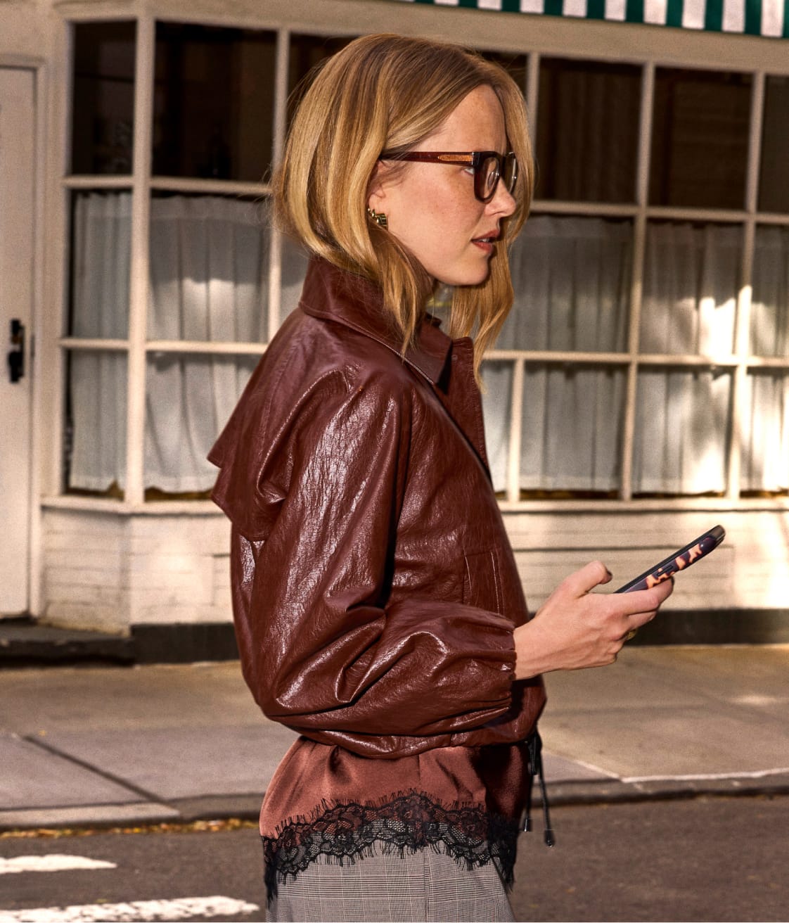 Woman wearing brown leather bomber jacket over a lace trim top and trousers. 