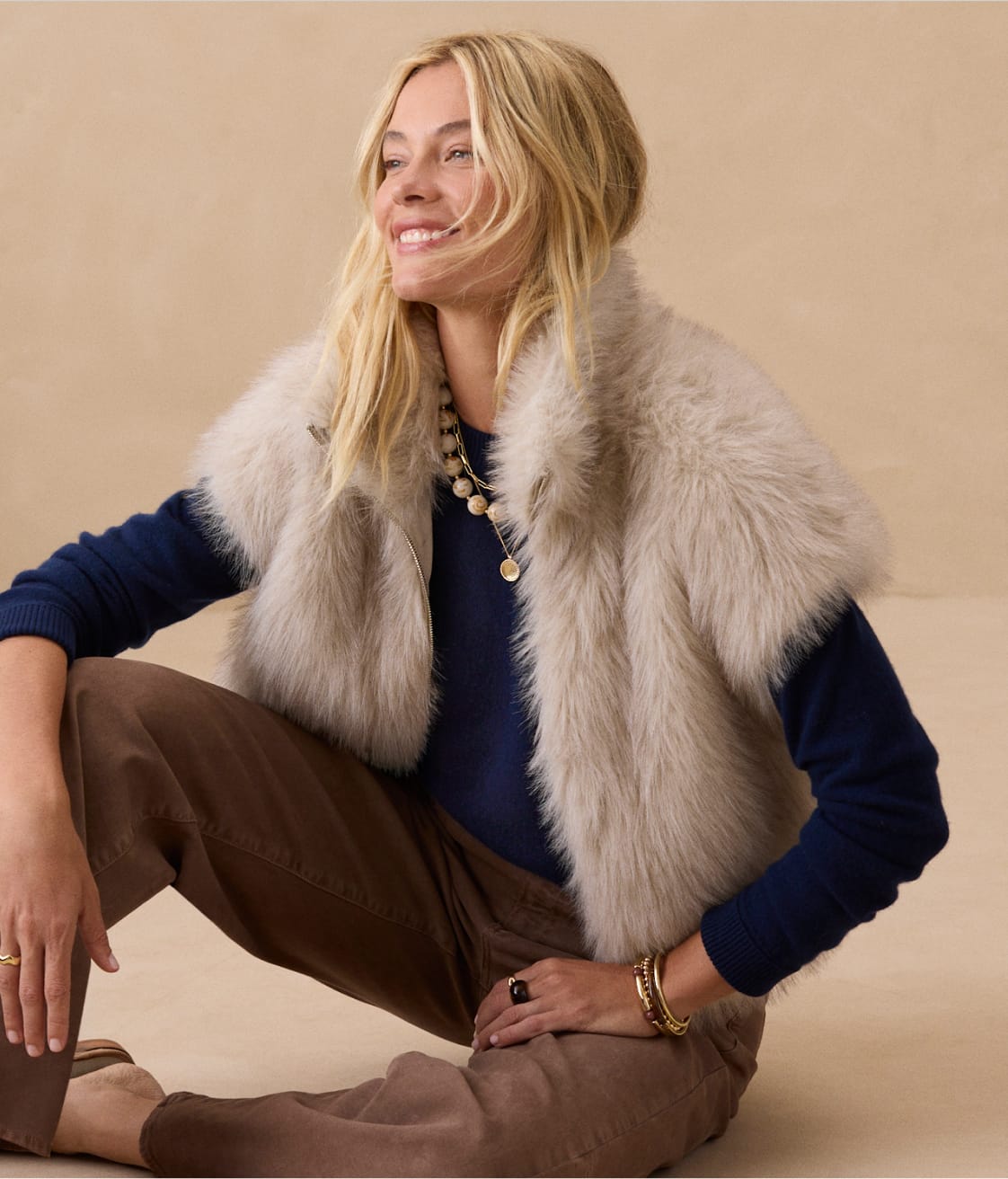 Woman wearing short sleeve fur jacket over a black knit top with brown wide leg pants
