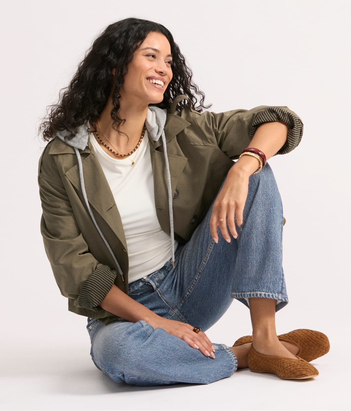 Woman wearing an olive green cropped trench coat over a white tee and blue jeans.
