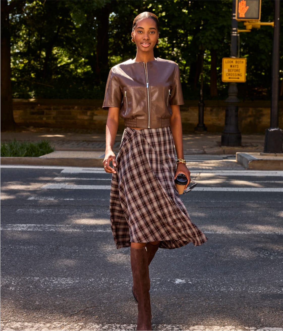 Woman wearing a brown short sleeve leather bomber jacket with a plaid midi skirt and boots. 