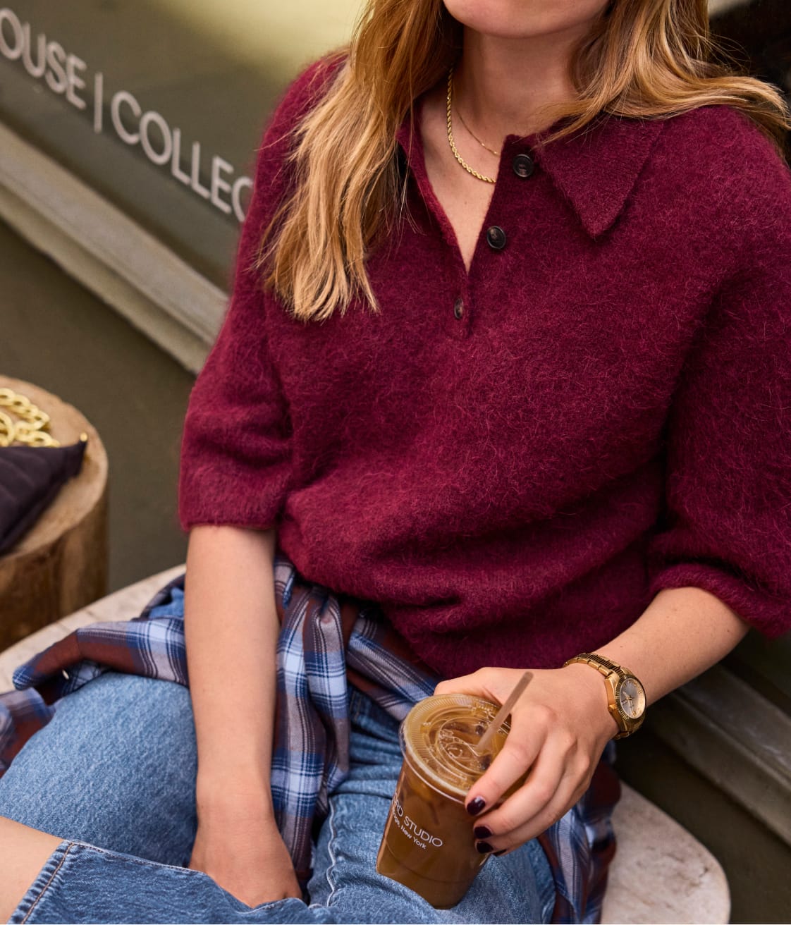 Woman wearing a maroon polo sweater with a plaid shirt tied at her waist and blue jeans.