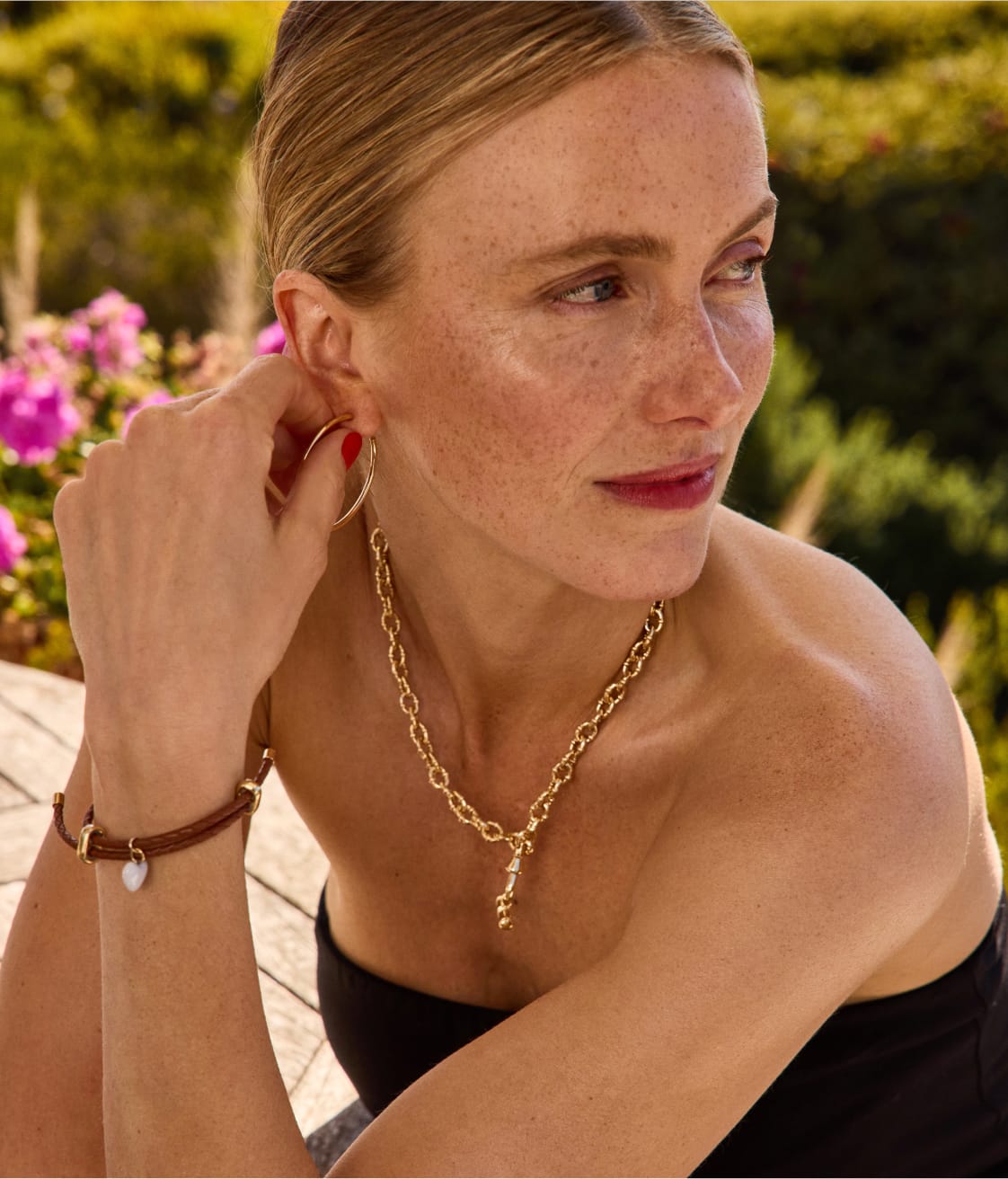 Woman wearing gold hoop earrings, a gold chain necklace, and a charm bracelet