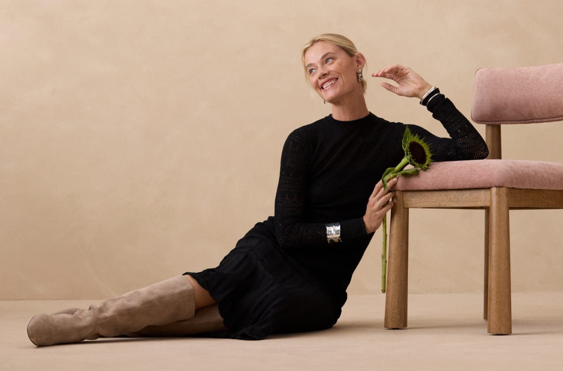 Woman wearing a fitted black midi dress with brown knee high boots