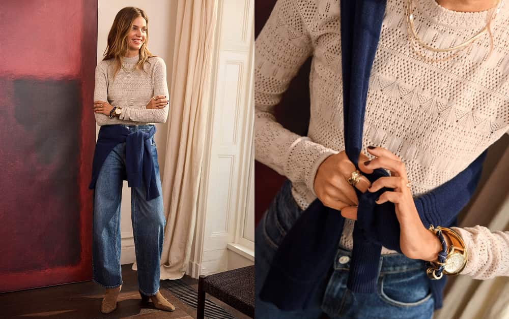 Woman wearing an ivory lacy top with a navy sweater and dark blue jeans