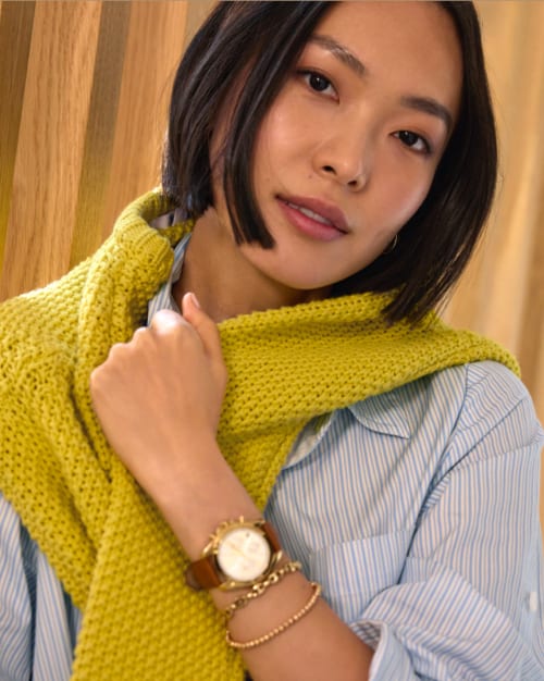 Image of woman wearing a blue stripe button down with a citron sweater draped over her shoulders